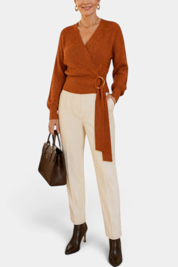Mahaute Zia rust orange wrap knit sweater with V-neck, tie waist, and long sleeves worn with cream trousers