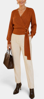 Mahaute Zia rust orange wrap knit sweater with V-neck, tie waist, and long sleeves worn with cream trousers