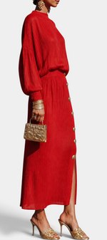 Mahaute red pleated two-piece set with a fluid blouse and long skirt featuring gold buttons and a side slit.