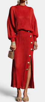 Mahaute Zornitsa red pleated two-piece set featuring a fluid blouse and a long skirt with gold button side slit.
